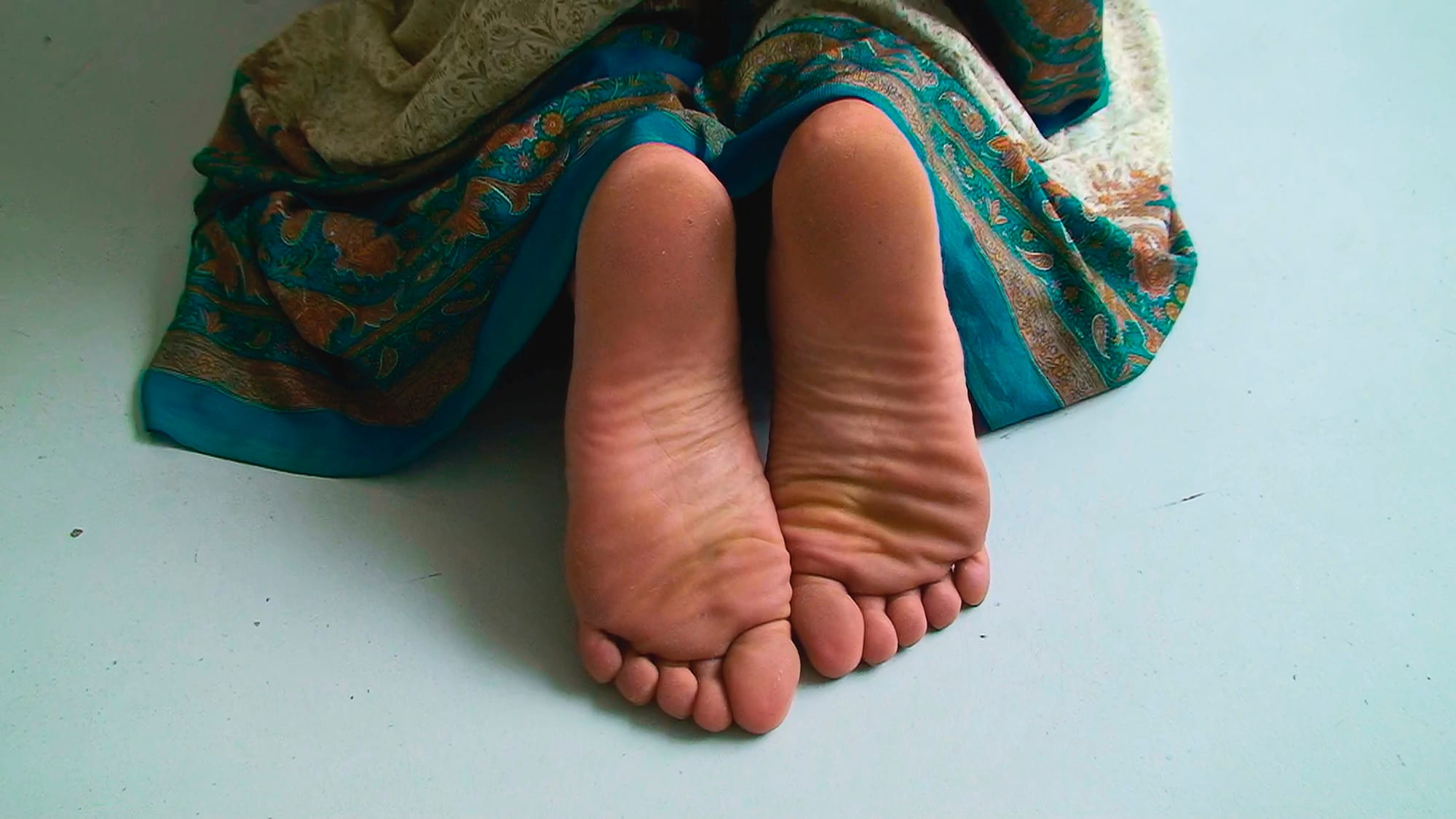 Video still: bare feet and a sari on a white floor. Afactum, 2007, Single-channel colour video projection, without sound, 3 min 58 s, projection size: 108 by 144cm