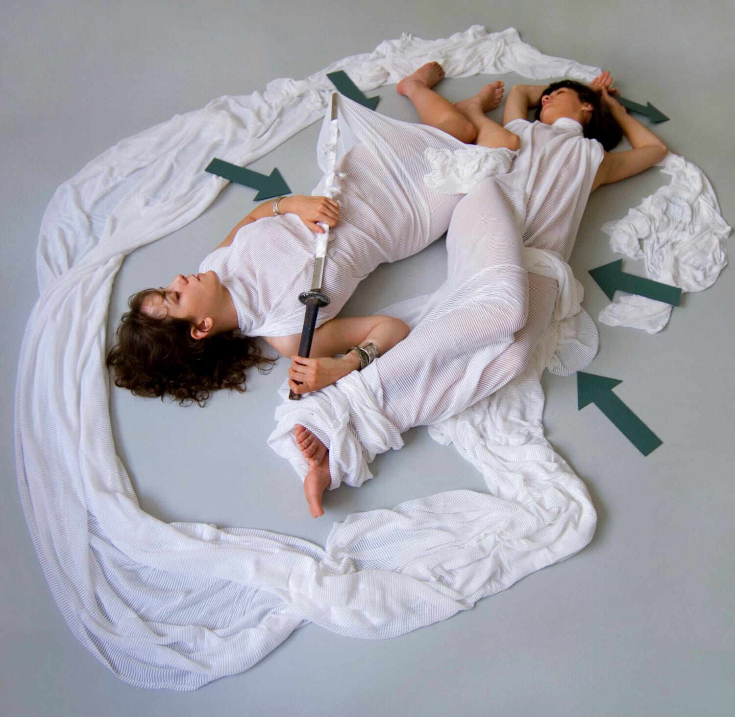 Two women lying in white fabric, with grey arrows pointing at them. afactum, 2009, Digital print on metal, Alu-Dibond, 50 x 50 cm
